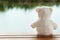 Lonely fluffy white bear doll sitting on wood terrace with water lake nature