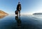 Lonely girl in black clothes with a bag standing on frozen Baikal lake on a sunny day