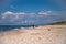 A lonely girl in a red jacket walks along a deserted sandy beach, on which sea foam waves roll.