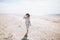 Lonely happy young woman in a hat and dress walks on a deserted sea beach on a sunny day. Summer vacation