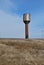 Lonely high rusty water tower in the field with dry grass and electricity line on the horizon, blue cloudy sky