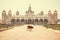 Lonely indian cow walking past famous building of the royal Palace of Mysore in Indo-Saracenic style, India.