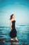 Lonely inspired woman in black dress staying on seaside dreaming and looking to sea on windy sunset day. Emotions loneliness
