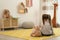 Lonely little girl with teddy sitting on floor at home, back view. Autism concept