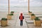 Lonely little kid in red sleeveless jacket with hood standing at deserted beach resort during off season dreaming concept
