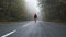 Lonely, lost tourist with black backpack walks on empty asphalt road