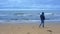 Lonely man in blue jacket with hood and jeans walks on beach