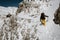 Lonely man climbs upside through the deep snow to the mountain hut on the edge of mountain using the ice ax during the sunny day