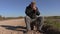 Lonely man with crutch sitting on suitcase on rural road