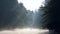 Lonely man with a paddle in the boat swimming on a calm river in dawn fog. The first rays of the morning sun make their