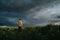 A lonely man in yellow jacket exploring rural area in Lithuania. Agricultural scene of rapeseed and dramatic storm clouds above.