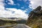 Lonely and moody road with clouds and an interesting light. Mountain road with dramatic colourful sky. Journey, outdoor, travel