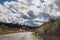 Lonely and moody road with clouds and an interesting light. Mountain road with dramatic colourful sky. Journey, outdoor, travel