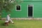 Lonely old man sitting on bench outside a green painted house