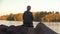 Lonely old woman sitting near lake and throwing stones solitude, back view