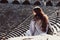 Lonely pretty young woman sits on the steps in ancient amphitheater on sunny day. European tourist back view