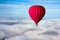 A lonely red hot air balloon floats above the clouds