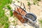 Lonely Rusty Wheelbarrow Sitting On The Sand With Small Grass Around