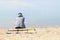 A lonely sad girl is sitting on the beach in a gray hoodie. Back view