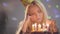 Lonely sad girl sitting in front of little cake lighting candles. Unhappy woman has birthday party. Concept of