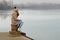 Lonely sad teenage girl sitting on dock on cold winter day