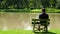 Lonely, sad young man sits on the edge of bench near lake in green park