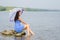 Lonely sad young woman with an umbrella sits on a rock by the river