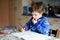 Lonely school kid boy at home making homework. Little child writing with colorful pencils, indoors. Elementary school