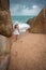 Lonely slender woman on a deserted beach on the background of large stones and a cloudy sky.