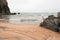 Lonely slender woman on a deserted beach on the background of large stones and a cloudy sky.