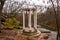 Lonely standing rotunda or round white gazebo on a granite slope of cliff on background of trees with fallen leaves and river, whi