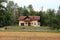 Lonely suburban family house with light pink facade and flowers on balcony surrounded with long driveway and tall forest