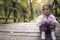 A lonely sweet little girl sitting on a small wooden bridge in t