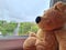 Lonely teddy bear sits window against blurred background of apartment building