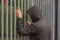 Lonely teenager sitting alone outside a metal fence with iron bars. Loneliness and bullying concept.