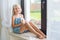 Lonely toddler russian girl sitting near window at home playing