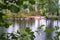 Lonely tourist sits on shore of a beautiful forest lake, in summer rain, in the foreground are blurry branches with