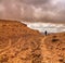 Lonely traveler is hiking on rocky desert. Snowing. Stormy heavy dark clouds above the mountains