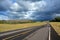 A lonely two lane road leads into a dark and stormy horizon