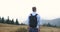 Lonely walk in the mountains. Handsome young man stands with a backpack on the top of a hill and looks thoughtfull at