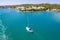 A lonely white yacht in the open sea sails to the picturesque shore with small white houses, Menorca, Spain, top view