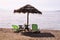Lonely wicker sun umbrella at beach by sea. Natural bamboo sunshades, summer umbrella parasol, deck chairs, table, sun bed.