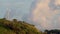 A lonely wind power generator standing on a mountain in a thicket of trees against a background of blue sky and beautiful cumulus