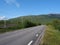 Lonely winding asphalt road and railroad in Abisko village and national park with birch forest and mountains, summer blue sky