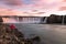 Lonely woman admiring a majestic waterfall glowing pink in midnight light