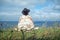 Lonely woman in felt hat and woolen poncho sitting on grassy seashore and looking out. View from behind. Travel, adventure,