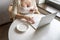 Lonely woman freelancer enjoying having breakfast with cup of coffee working on laptop sitting near window in cafe at morning.