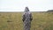 Lonely woman in a long camouflage jacket walks along a large field. Walk in a non-standard place.