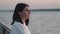 A lonely woman standing on the embankment of the city river and looking on waves. Headshot Portrait of Pensive