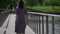 lonely woman is walking on bridge over river at summer day, rear view